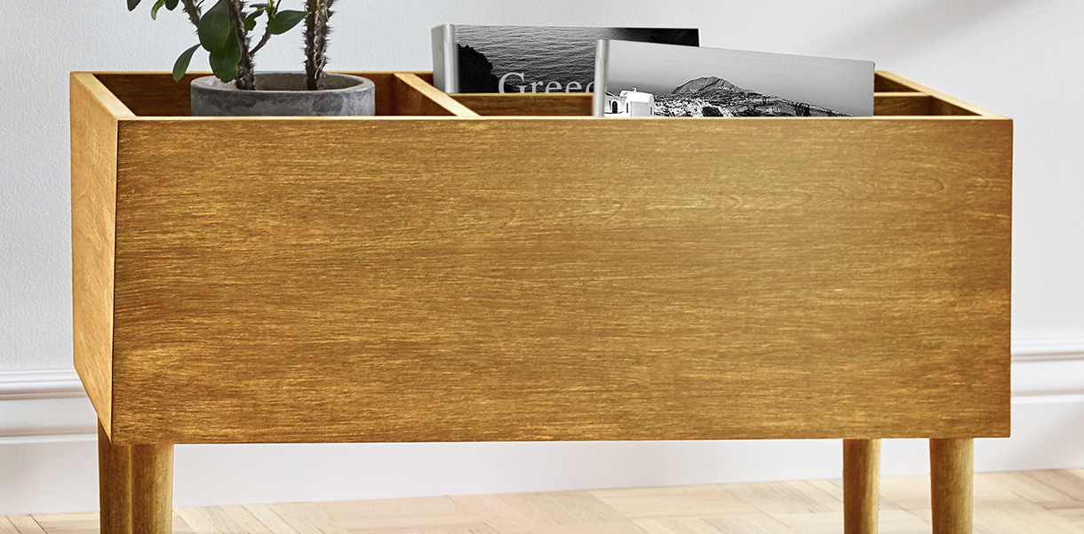 A magazine rack in a living room, treated with Minwax Polyshades in satin Honey Pine, contains a potted plant and books.